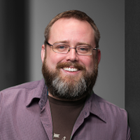 Headshot of Adam Wilbert, a dapper man with a graying beard